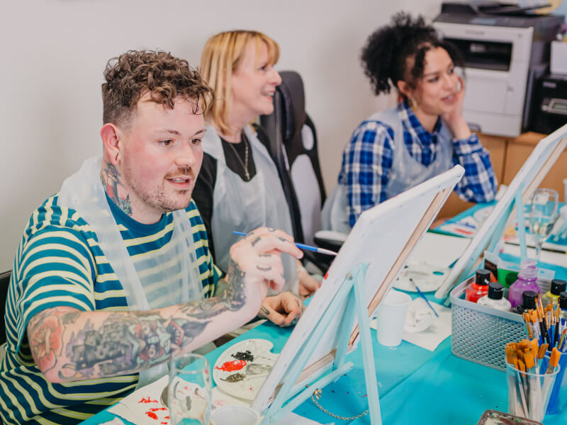 Art class with man in focus painting on a canvas